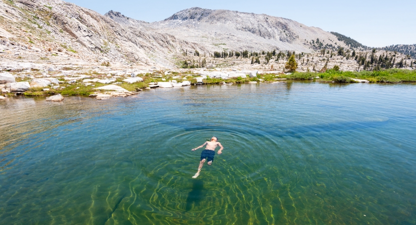A person floats on their back in an alpine lake with bare mountains in the background. 